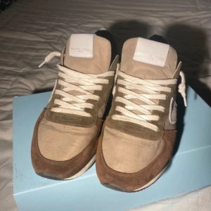 Sneakers från Philippe Model - Snygga sneakers från Philippe Model i beige och brunt mocka med vita snören. Skorna har en rund tå och en stilren design som passar perfekt för en avslappnad look. De kommer i originalförpackning.