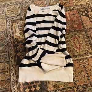 Randig stickad tröja från Zara - Säljer en beige och svart randig stickad tröja från Zara i storlek S. Tröjan har långa ärmar, rund halsringning och breda ribbade muddar vid ärmslut och nederkant. Perfekt för en avslappnad och trendig look.