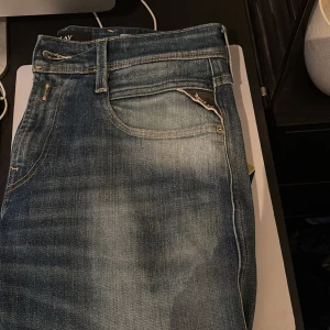 Blå Replay Anbass jeans slim fit - Säljer ett par blå Replay Anbass jeans i slim fit med klassisk femficksdesign och snygga slitningar. Jeansen har dragkedja, läderpatch bak och är tillverkade i stretchigt denim för extra komfort. Midjemått W30.