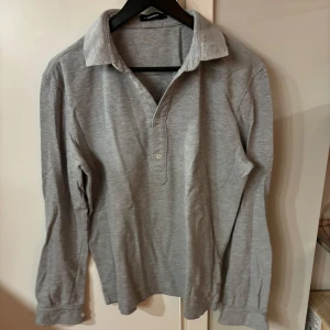 Grå långärmad pikétröja från J.Lindeberg - Säljer en stilren grå långärmad pikétröja från J.Lindeberg. Tröjan har klassisk krage, knappar framtill och är tillverkad i mjukt bomullsmaterial. Perfekt för en avslappnad men snygg look eller när du spelar golf. Storlek herr M men är snygg lite oversize på mig som brukar ha dam S. 