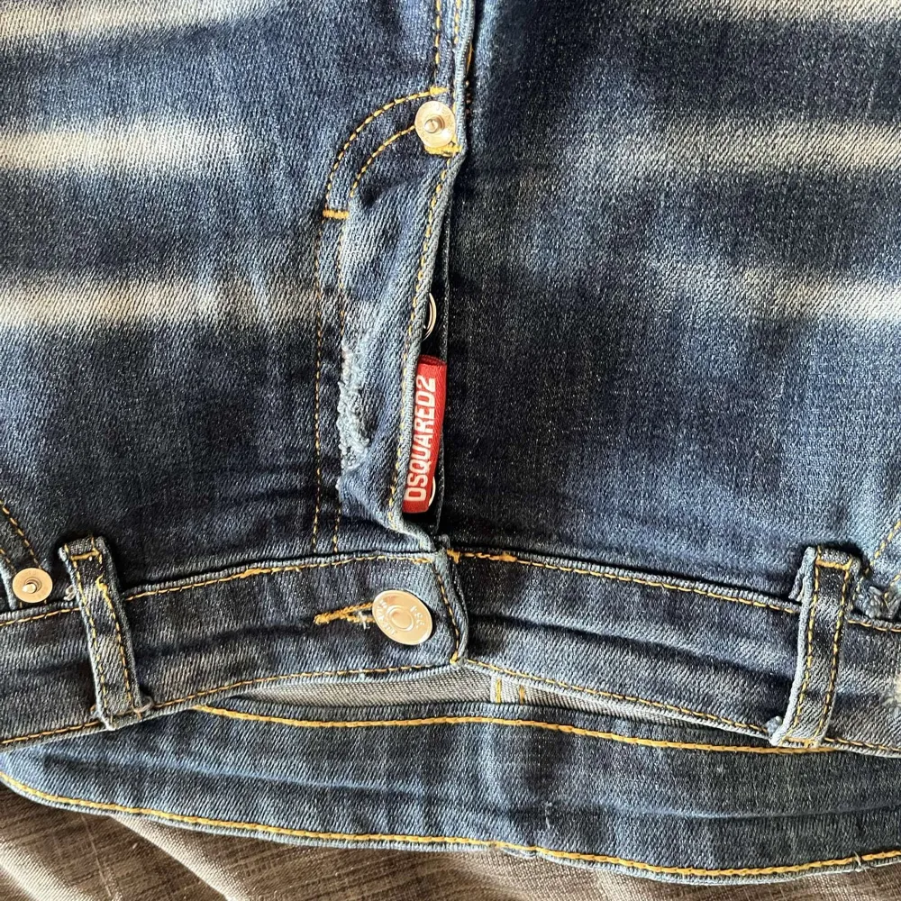 Säljer ett par blå jeans från Dsquared2 med slitningar och hål på knäna. Jeansen har slim passform, klassisk femficksdesign och tydliga slitdetaljer framtill. Perfekta för en avslappnad och trendig look.. Farkut & Housut.