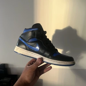 Nike Air Jordans i svart och blått - Snygga Nike Air Jordans i svart och blått med klassisk snörning. Skorna har en rund tå och en ikonisk design med blå detaljer på sidorna och hälen. Perfekta för dig som vill ha en stilren look med en sportig touch.använts ett par gånger bara.ingen original förpackning 