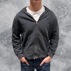 Ralph Lauren Full-Zip Hoodie Grå - •Ralph Lauren Full-Zip Hoodie Grå. Skick: 7-8/10, en liten lagning på luvan (ej särskilt märkbart vid användning), se sista bild! Storlek: 14/16 år, = 155-165 cm~. Modell: 173 cm, 65 kg. Sitter för litet på modellen på bild! Authentic: ✅. Hör av dig vid frågor eller funderingar, mvh Hessler’s;)