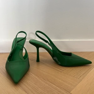 Gröna pumps med klack från Zara - Säljer ett par stilrena gröna pumps från Zara med spetsig tå och öppen häl. Skorna har hög klack och en elegant siluett, perfekta för att sticka ut. Färgen är en klar grön.