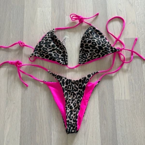 Leopardmönstrad bikini med rosa detaljer - Trendig bikini med leopardmönster och knallrosa detaljer. Överdelen har knytband och trekantsform, medan underdelen är en trosa med hög skärning. Endast testad men fel storlek för mig. Storlek är M mer är mer som en L. (Sista bild lånad)