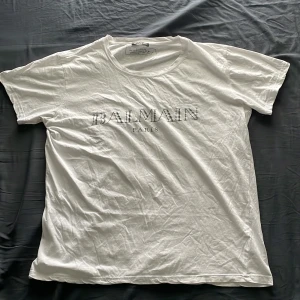Vit t-shirt från Balmain Paris - Vit t-shirt från Balmain Paris med tryckt logga på bröstet. Klassisk rund halsringning och korta ärmar. Perfekt för sommaren. Den är storlek L men den är liten i storleken så skulle säga att den är mer en M