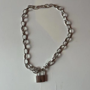 Silverfärgat halsband med hänglås - Kedjehalsband i silverfärg med ett coolt hänglås som detalj. Perfekt accessoar för att ge din outfit en edgy vibe. Passar både till vardags och när du vill sticka ut lite extra. Helt oanvänt