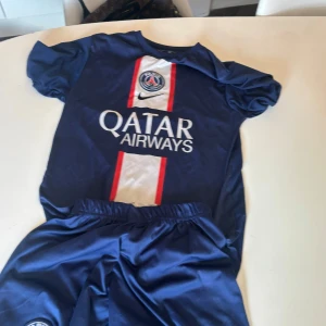 Blå PSG fotbollströja med shorts - Säljer en blå PSG fotbollströja med korta ärmar och matchande shorts. Tröjan har vit och röd detalj på framsidan med Qatar Airways-logga. Baksidan har spelarnamnet och numret 7. Perfekt för fotbollsfans!