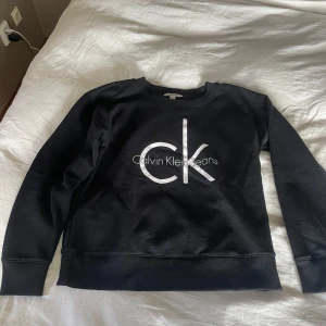 Svart sweatshirt från Calvin Klein Jeans - Säljer en stilren svart sweatshirt från Calvin Klein Jeans med det ikoniska CK-logotypen i vitt på framsidan. Tröjan har långa ärmar och en rund halsringning. Perfekt för en avslappnad look.