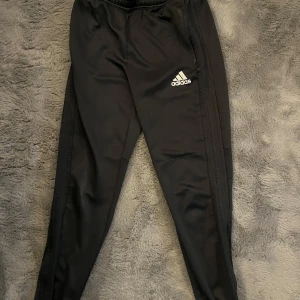 Svarta träningsbyxor  ”Adidas” - Säljer ett par svarta träningsbyxor från Adidas med elastisk midja och det klassiska logotyptrycket på benet. 