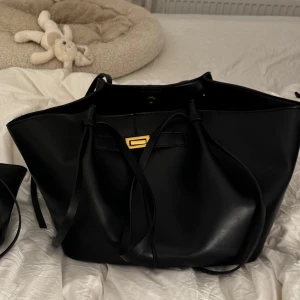 Svart axelväska med gulddetalj - Elegant svart axelväska i skinn med en stilren design. Väskan har en gulddetalj på framsidan och långa handtag för bekväm bärning. Perfekt för att bära med sig det nödvändigaste med stil. Pris för båda 700kr 