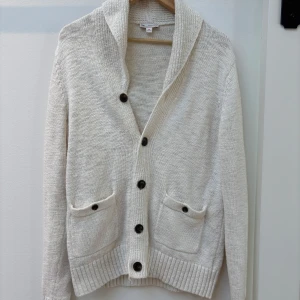 Vit stickad kofta från Gap - Säljer en vit stickad kofta från Gap i storlek M. Koftan har stora knappar framtill, två fickor och en bred krage. Perfekt för lager-på-lager och passar till många olika stilar.