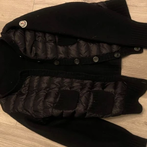 Svart cardigan jacka från Moncler - Snygg svart cardigan jacka från Moncler med  knappar framtill, perfekt för sommaren . Köpt från vinted. Den är i bra skick och används fåtalsgånger. Den jag köpte den av har råkat krymt den i tvätten så den motsvarar storlek Xs. Men jag som har S kan ha den! Ena armen är lite större och puffigare än den andra men fortfarande jätte fin