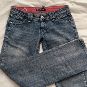 Lågmidjade jeans  - Snygga lågmidjade blå jeans med en klassisk femficksdesign och knappgylf. De har en normal booutcut passform och är perfekta för en avslappnad stil. Insidan av linningen har en röd detalj som ger en extra touch.
