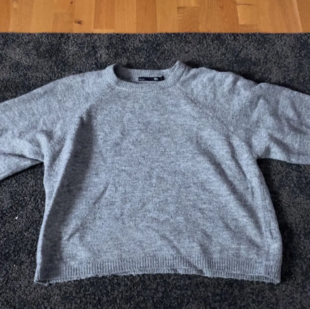 Mysig grå stickad tröja med rund halsringning och långa ärmar. Perfekt för kyligare dagar och enkel att matcha med olika outfits.. Neuletakit & Villapaidat.