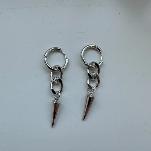 Silvriga örhängen med nitar - Säljer ett par coola silvriga örhängen med kedjelänkar och en spetsig konformad hängande detalj. Passar till både vardag och när du vill sticka ut lite extra. Säljer då jag endast använder guldsmycken 🥰Aldrig använda.
