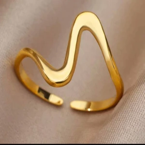Guldfärgad vågig ring - Trendig ring i guldfärg med vågig, öppen design. Perfekt för dig som vill ha ett unikt och stilrent smycke som sticker ut. Passar att bära ensam eller att kombinera med andra ringar.