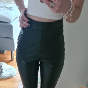Svarta skinnbyxor med hög midja - Säljer ett par svarta bootcut skinnbyxor med hög midja. Byxorna har en stilren look utan synliga detaljer och sitter tight upptill men är vidare nertill. Perfekta för dig som vill ha en edgy och trendig stil. Sälj för dom kommer inte till användning!💕