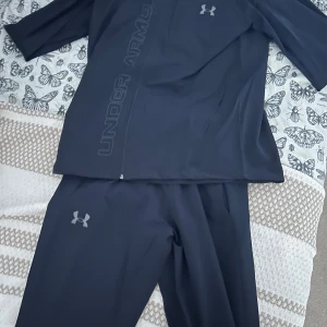 Svart träningsdress från Under Armour - Säljer en svart träningstracksuit från Under Armour i helt nytt skick. Perfekt för träning och har en stilren design med lång ärm. I storlek S. Har aldrig använt den, Så tveka inte på att höra av er 