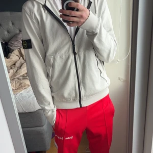 Vit zip-hoodie från Stone Island 100% ÄKTA - Vit hoodie med dragkedja från Stone Island. Klassisk patch på vänster ärm, två fickor fram och ribbade muddar. Perfekt för en avslappnad stil och enkel att matcha med andra plagg.