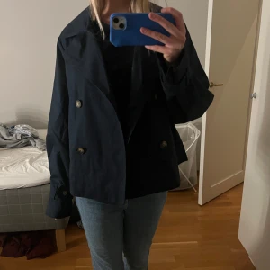 Mörkblå kavajjacka från NA-KD - Säljer en mörkblå trenchcoat från NA-KD med dubbelknäppning och bred krage. Jackan har en rak, något oversized passform. Perfekt nu till våren. Använd mycket fåtal gånger