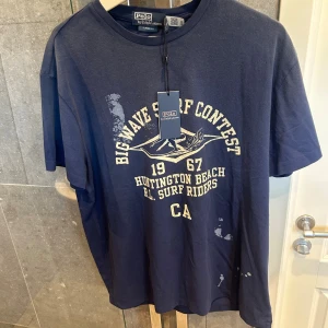 Blå t-shirt Polo Ralph Lauren - Snygg mörkblå t-shirt från Polo Ralph Lauren som är väldig unik i storlek M, helt ny och ny pris ligger på 1800kr! Kom gärna med pris förslag och frågor!