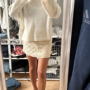 Beige broderad minikjol från Zara - Superfin beige minikjol från Zara med broderade detaljer och pärlor. Kjolen har ett unikt mönster med små blommor och pärlbroderier som ger en lyxig känsla. Perfekt för dig som vill sticka ut med en snygg och trendig look.