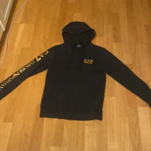 Svart EA7 hoodie med guldtryck - Säljer en EA7 hoodie. Den är väldigt bra skick. Kom privat för mer frågor. Pris kan diskuteras vid snabb affär. 