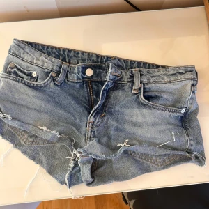 Blå jeansshorts - Snygga blå jeansshorts med fransig och rå kant nertill. Klassisk femficksmodell med knapp och dragkedja framtill samt bälteshällor. Perfekt för dig som gillar en avslappnad och cool stil på sommaren.