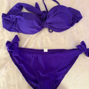 Lila bikini med knyt XL underdel - Snygg lila bikini i storlek XL med knyt på underdel. Ingen aning vad överdelen är i för storlek tyvärr. Bikinin har en bandeau-topp med knyt framtill och matchande trosor med rosett på sidorna. Tillverkad i 100% bomull, perfekt för strandhäng och poolparty.