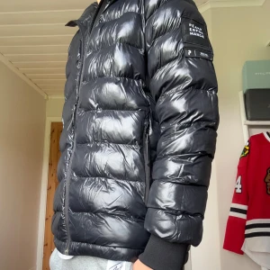 Svart pufferjacka Peak Performance - Säljer min riktigt feta, svarta, glansiga pufferjacka från Peak Performance med huva och dragkedja. Jackan har en quiltad look, ribbade muddar och logotyp på ärmen. Det är en snygg vinter vinterjacka, som passar under kalla dagar. Är i fint skick. Hör av er vid frågor eller funderingar:)