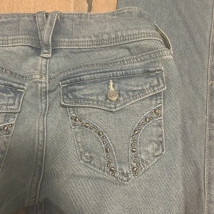 Ljusblå bootcut jeans Hollister - Snygga ljusblå bootcut jeans från Hollister med låg midja. Jeansen har coola detaljer med nitar på bakfickorna och klassisk femficksdesign. Materialet är mjukt denim och passformen är riktigt skön. Perfekta för dig som gillar en avslappnad men trendig stil. Helt nya använda 2ggr max. Köpt på påsklovet när jag va i nyc.(PRIS KAN DISKUTERAS)
