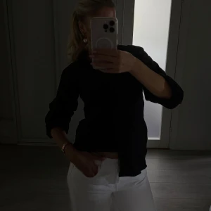 Svart skjorta med smockad midja - Svart skjorta i bomull med klassisk krage och långa ärmar. Skjortan har knappar framtill och en smockad detalj i midjan som ger en snygg passform. Perfekt till jeans eller kostymbyxor för en clean look. En knapp har lossnat, men inget man lägger märke till