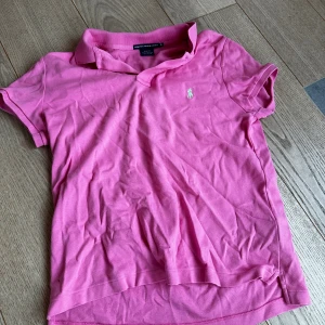 Rosa pikétröja från Ralph Lauren Sport - Säljer en rosa pikétröja från Ralph Lauren Sport i storlek XL. Tröjan har klassisk krage, korta ärmar och den ikoniska broderade loggan på bröstet. Slim fit-modell i 100% bomull, perfekt för en chill och stilren look.