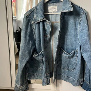 Jeansjacka från Carin Wester, blå - Snygg klassisk jeansjacka från Carin Wester i ljusblå denim. Jackan har stora framfickor, knappar framtill och en cool krage. Perfekt för dig som gillar en chill och tidlös stil. Passar lika bra till hoodie som till t-shirt.