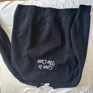 Svart sweatshirt med vit text - Svart sweatshirt med vit broderad text på framsidan och baksidan. Texten har ett statement-tryck med budskap om kärlek och mot diskriminering. Tröjan har rund hals och långa ärmar, perfekt för dig som vill ha en chill och snygg look.