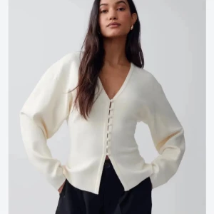 Vit kofta med v-ringning och knappar - Snygg vit kofta med v-ringning och dekorativa knappar framtill. Modellen har långärmad passform och är tillverkad i ett mjukt stickat material. Perfekt att styla med jeans eller kjol för en clean look. Slutsåld❤️❤️❤️