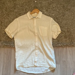 Beige kortärmad skjorta från !Solid - Snygg beige skjorta från !Solid med korta ärmar och klassisk krage. Skjortan har bröstficka och knäppning framtill. Regular fit för en avslappnad look, perfekt till sommaren. Tillverkad i ett lätt linnematerial som andas.