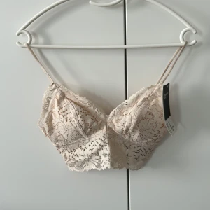 Beige spets bandeau topp H&M XS - Supersöt bandeau topp från H&M i beige spets med tunna axelband och avtagbara inlägg. Toppen har ett romantiskt blommigt spetsmönster och en liten rosett bak. Perfekt att styla under en öppen skjorta eller kavaj. Pris 100kr, ordinarie 149kr