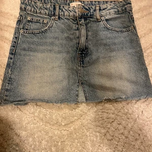 Jeanskjol från Gina Tricot - Snygg ljusblå jeanskjol från Gina Tricot med rå kant nertill och klassiska femficksdetaljer. Kjolen har en normal passform och är perfekt för dig som gillar en avslappnad och trendig stil. Dragkedja och knapp framtill.
