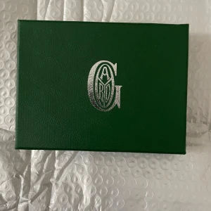 Grön Goyrad plånbok med mönster - Säljer en snygg grön plånbok från Goyrad med deras ikoniska grafiska mönster. Plånboken är i skinn och har flera fack för kort. Kommer i originalask med gul putsduk och äkthetskort. Perfekt accessoar för dig som gillar lyxiga detaljer.