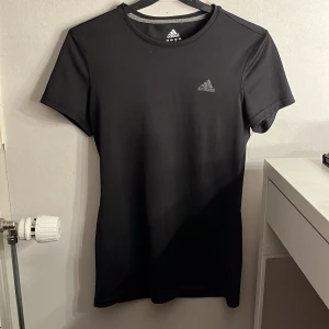 Svart Adidas Climalite t-shirt - Svart t-shirt från Adidas med diskret logga på bröstet. Modellen är klassisk med rund hals och korta ärmar. Tillverkad i Climalite-material som andas och passar perfekt för träning eller sportiga outfits. Aldrig använd!