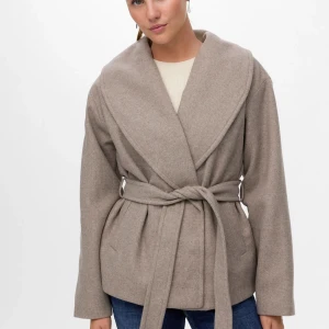 Beige omlottjacka med bälte från Vero Moda - Snygg beige omlottjacka från Vero Moda med bred krage och knytskärp i midjan. Inga defekter och den är i mycket bra skick. Nypris - 749kr