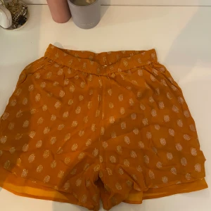 Gula prickiga shorts från DAY - Snygga gula shorts från DAY med glittriga prickar i guld. De har elastisk midja och är tillverkade i ett lätt och luftigt material, perfekta för varma dagar. Shortsen har en loose passform och ger en cool och trendig vibe. Kan vikas ner så de blir mer lågmidjade