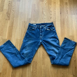 Levi's 501 blå jeans W29 L32 - Klassiska Levi's 501 jeans i blå denim med raka ben och normal passform. Byxorna har fem fickor, knappgylf och den ikoniska läderpatchen bak i midjan. Perfekta för dig som gillar tidlös stil och vill ha ett par riktigt schyssta jeans.😘.   Nypris 1200kr
