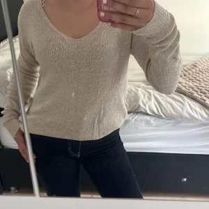 Beige stickad tröja med v-ringning - Mysig beige stickad tröja med v-ringad hals och långa ärmar. Tröjan har en enkel och stilren design som är lätt att matcha med olika outfits. Perfekt för dig som gillar en avslappnad och klassisk look.