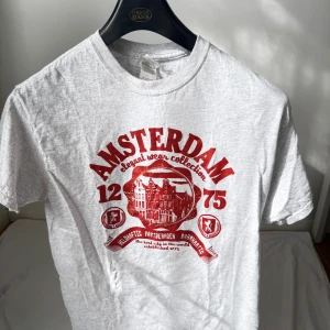 Amsterdam t-shirt med rött tryck - Snygg ljusgrå t-shirt från Dressmann med stort rött Amsterdam-tryck på bröstet. Klassisk rund hals och korta ärmar. Materialet är mjuk bomull med lite polyester, perfekt för chill dagar. Trycket har coola detaljer med text och grafik.