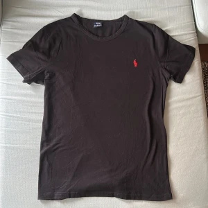 Svart t-shirt från Polo Ralph Lauren - Svart t-shirt från Polo Ralph Lauren med klassisk röd broderad logga på bröstet. Den är i storlek M men passar även M. Säljer eftersom att den är för liten för mig, har bara haft på mig den en gång. Priset går att diskutera vid snabb affär.
