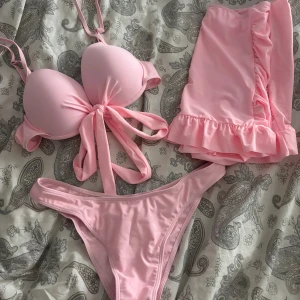 Ljusrosa bikini med volangkjol - Supersöt ljusrosa bikini med vadderad topp och knyt framtill. Matchande trosor med hög benskärning och en volangprydd kjol 