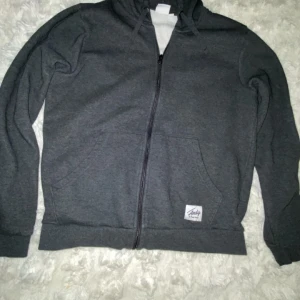 Mörkgrå hoodie med dragkedja - Mörkgrå hoodie från Andy med hel dragkedja framtill, huva med snörning och två stora fickor. Tillverkad i mjukt bomullsmaterial, Strl M